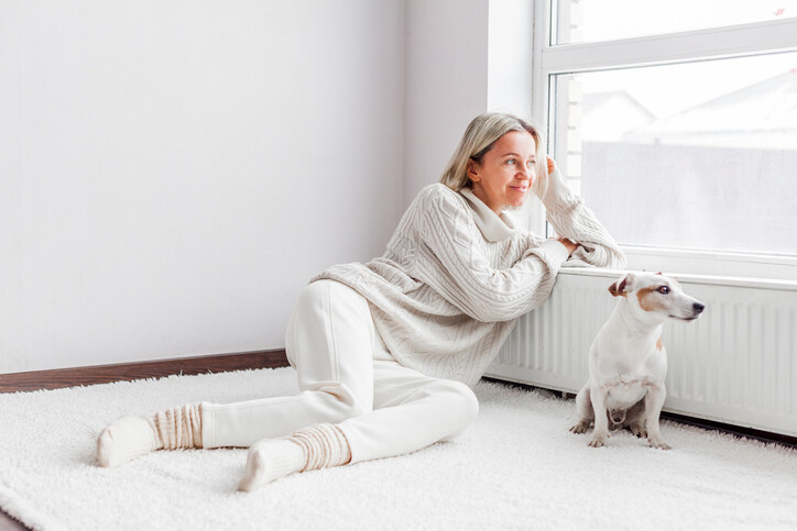 Frau sitzt entspannt mit ihrem Hund am Fenster und genießt die wohlige Wärme in ihrem Zuhause durch dichte Fenster