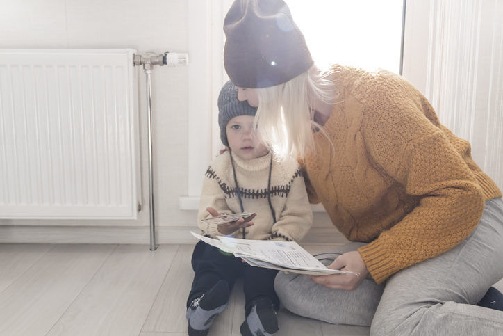 Frau und Kind sitzen mit Pullover und Mütze im kalten Zuhause und sind entsetzt über die hohen Kosten für Energie und Heizung