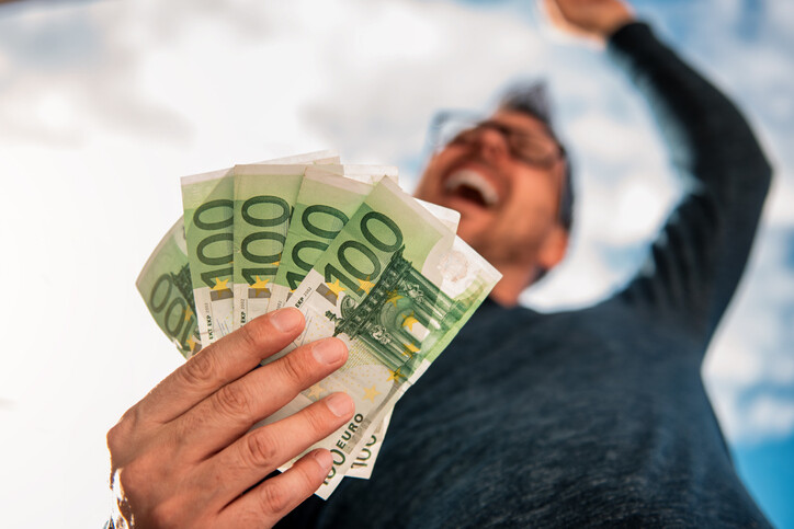Mann hält 100 Euro Scheine in der Hand und freut sich über die Kosteneinsparung